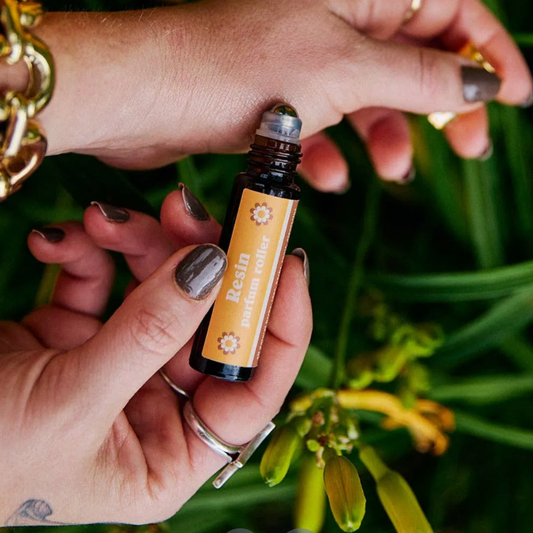 Hand holding a small bottle labeled 'Resin' against a green plant background