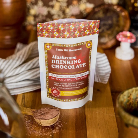 Packaging of Cedar Hill Homestead Mushroom Drinking Chocolate on a wooden surface with a spoonful of chocolate.